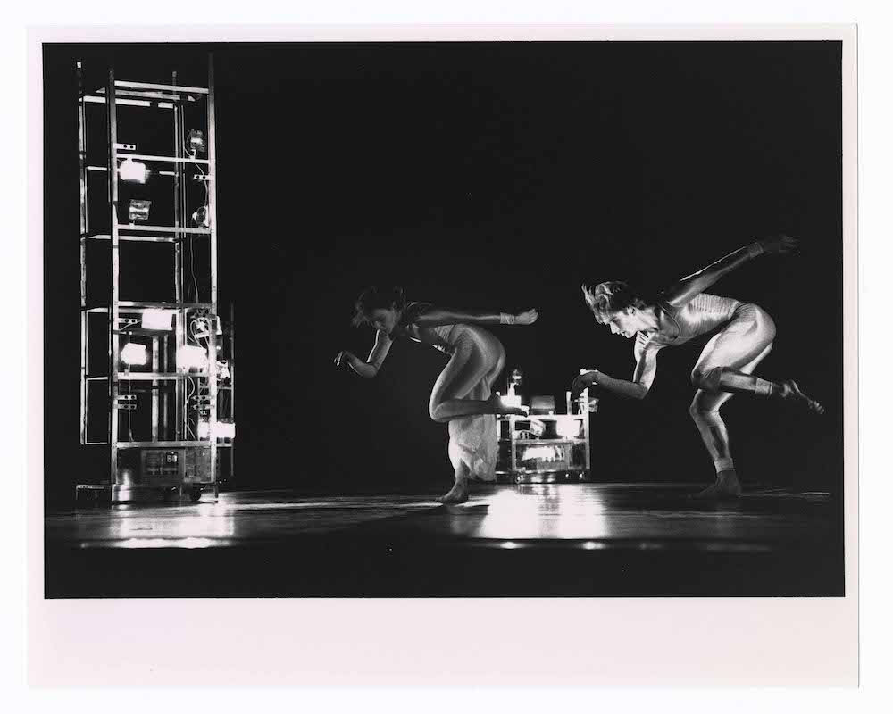 two dancers in a huddled over jump being lit by Robert Rauschenberg's towers