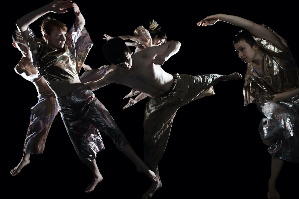 dancers in glittery costumes fly through the air en masse. their bodies create a beautiful sculpture