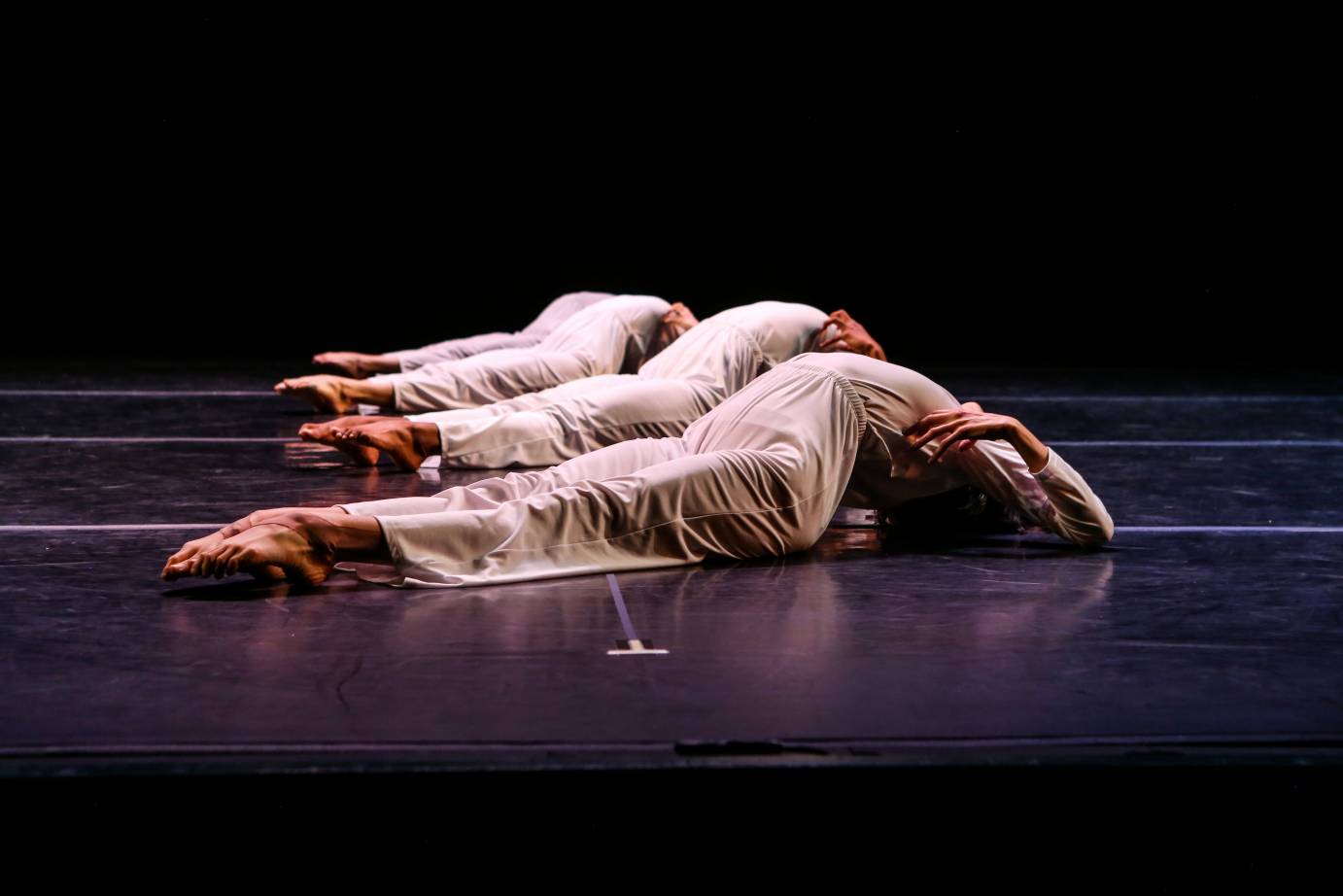 4 Dancers dressed in silky white lie on the black floor and arch their backs