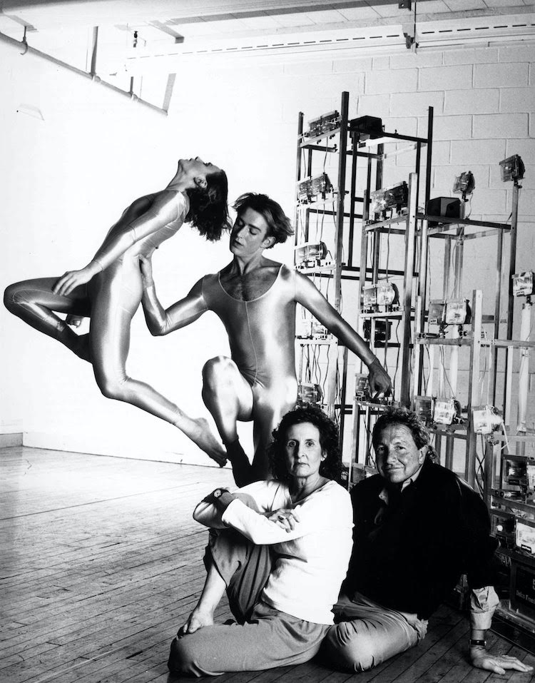 photo of Trisah Brown and Robert Rauschenberg in a studio. Behind them are towers built for Astro Converted and two dancers dancing.
