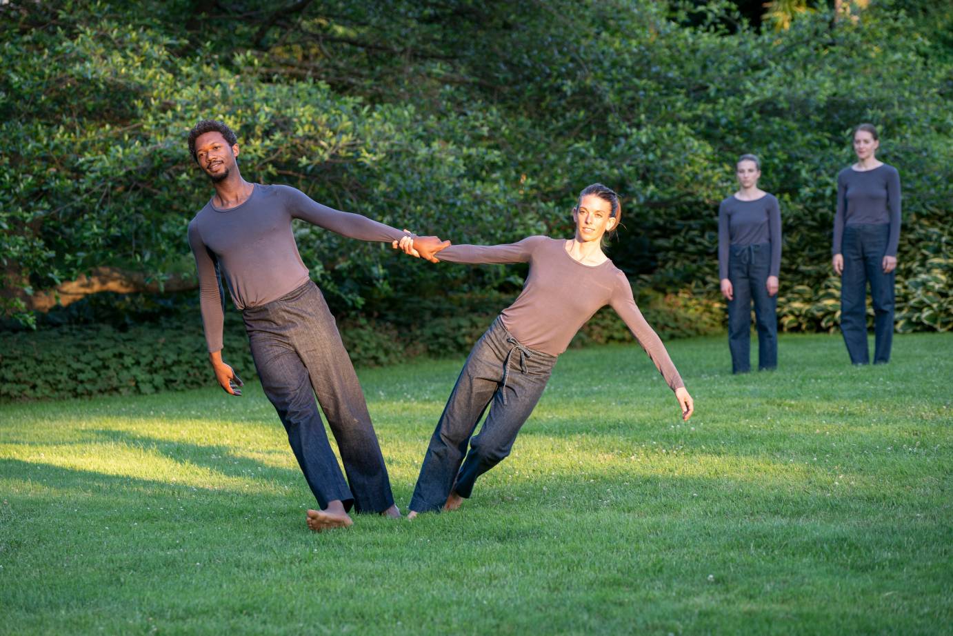 A man and a woman hold hands and lean away from each other as two dancers watch behind them