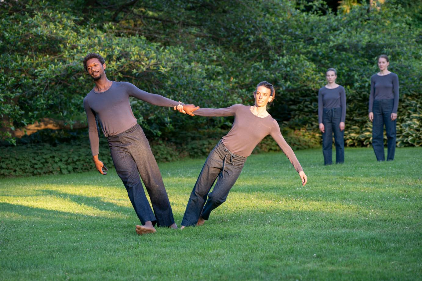 A  man and a woman hold hands and lean away from each other as two dancers watch behind them