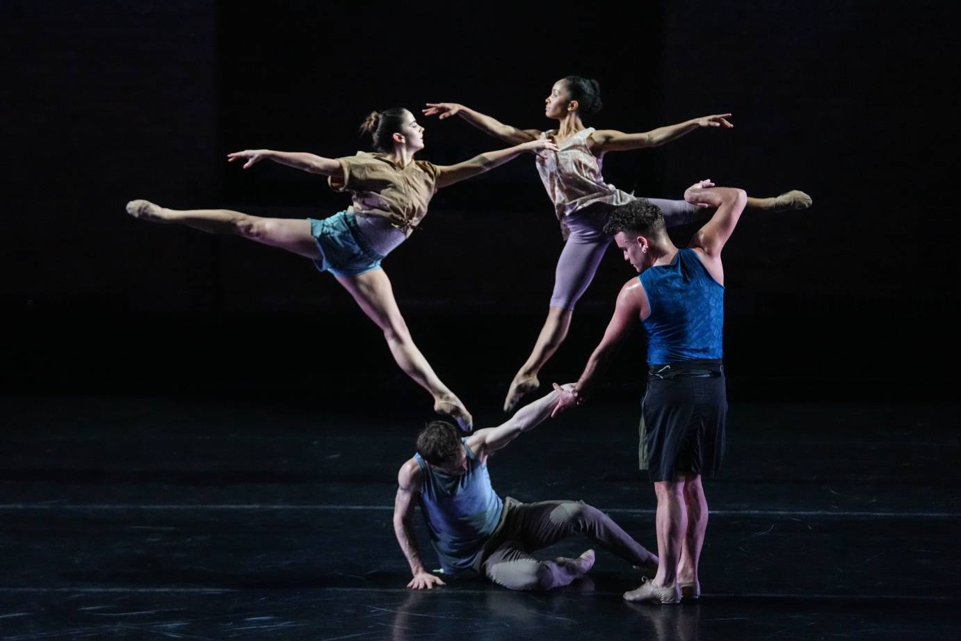 2 dancers jumping behind a crouched dancer in the foreground. A standing dancer holds his hand