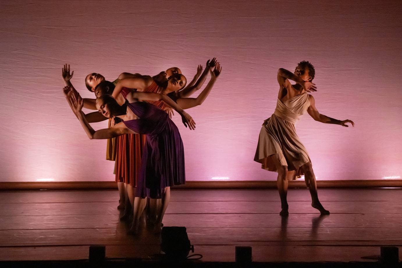 One female dancer to the left of a group of dancers, their arms making S curve shapes