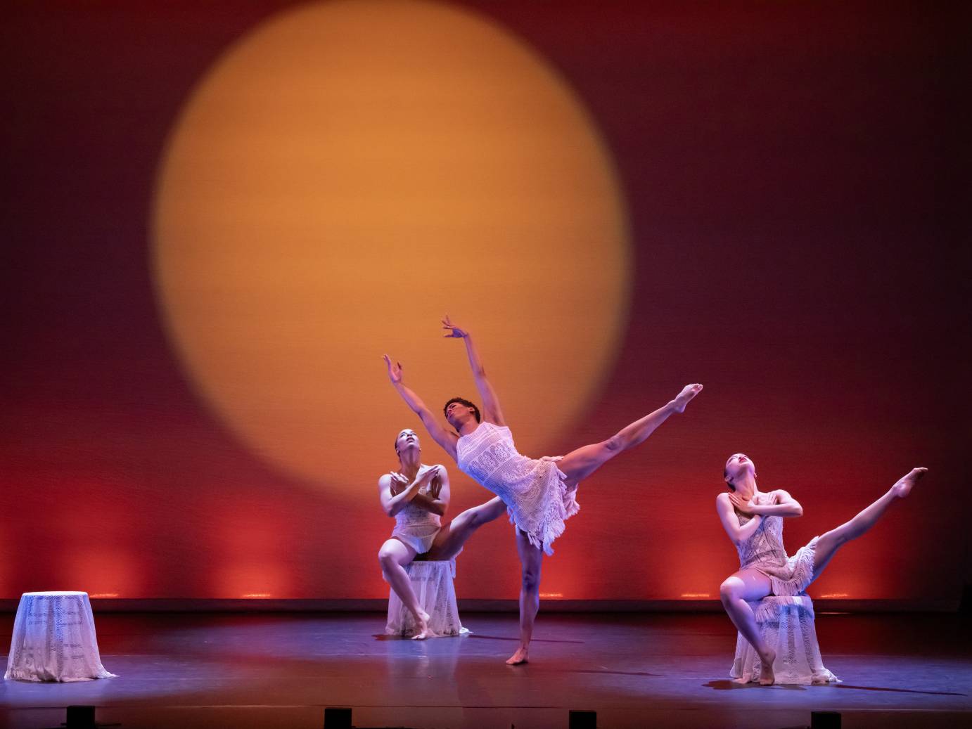 3 female dancers pose with one leg extended. 2 are seated one is standing