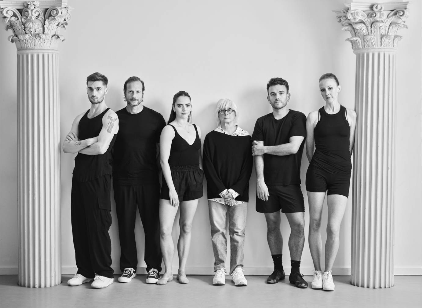 Black and white photo of Twyla Tharp and 5 dancers standing in a line between 2 ornate pillars