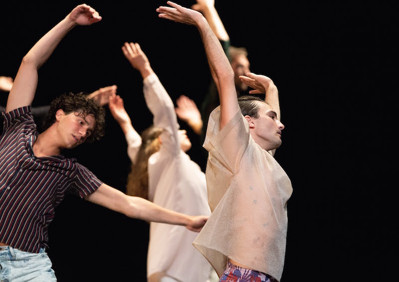 Dancers in stripes and sheer, soft colored tops outstretch their arms above their heads and to their sides