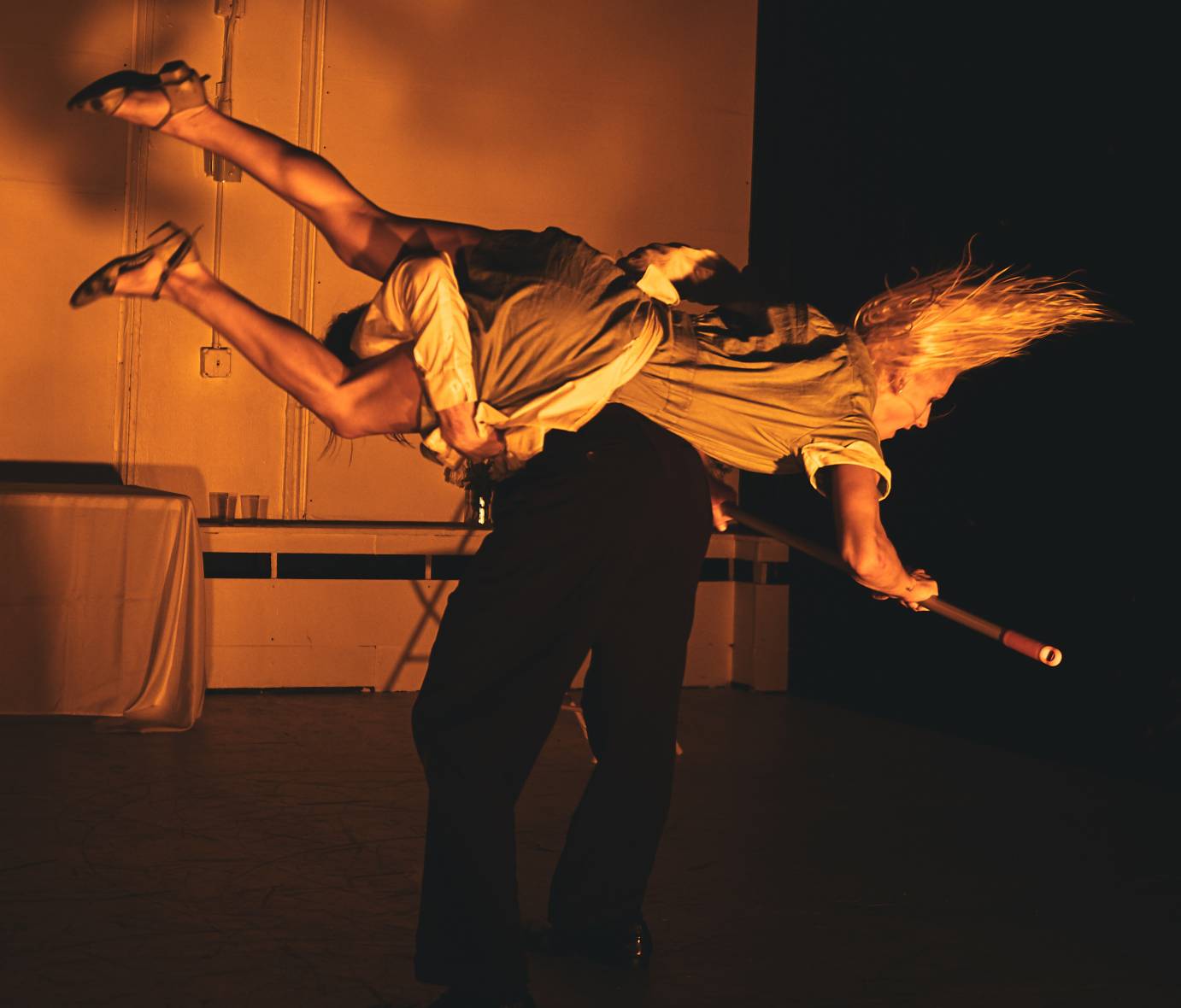 A man lifts a mop-holding woman around his back