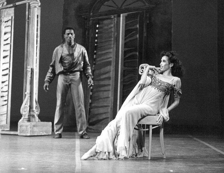 black and white photo, a set of louvered dours with Lowell Smith in street clothes emanating strength while Virginia Johnson sits on a chair looking crazed and disheveled