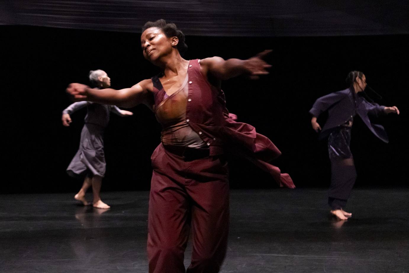 Three performers caught in the middle of turning, form a triangle. A woman with a beautific facial expression is foreground.