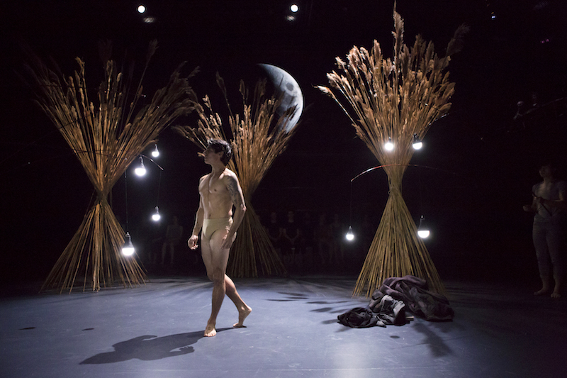 Joaquin De Luz stands in briefs amongst corn stalk set pieces.