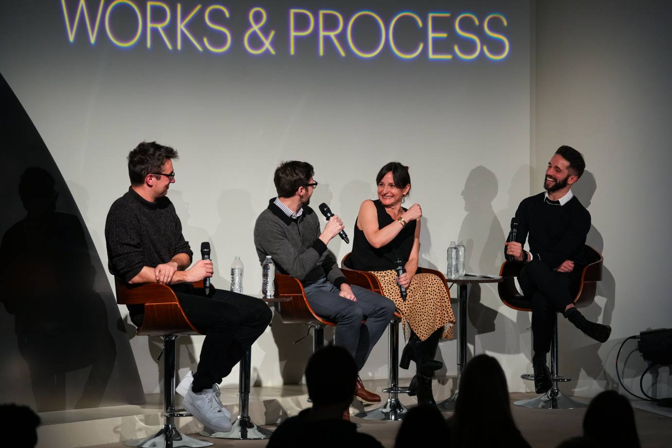 Works & Process, Guggenheim Museum sign below which sit Ellis Ludwig-Leone looking at Troy Schumacher who is speaking with a smiling Karen Russell. Her right arm is folded across her body and she is slightly leaning back. Michael Sean Breeden, bearded with arms folded looks on amusedly