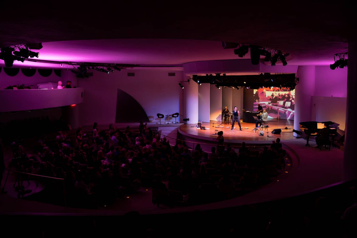 The stage seen from afar. Purple light surrounds the stage as the performers perform.