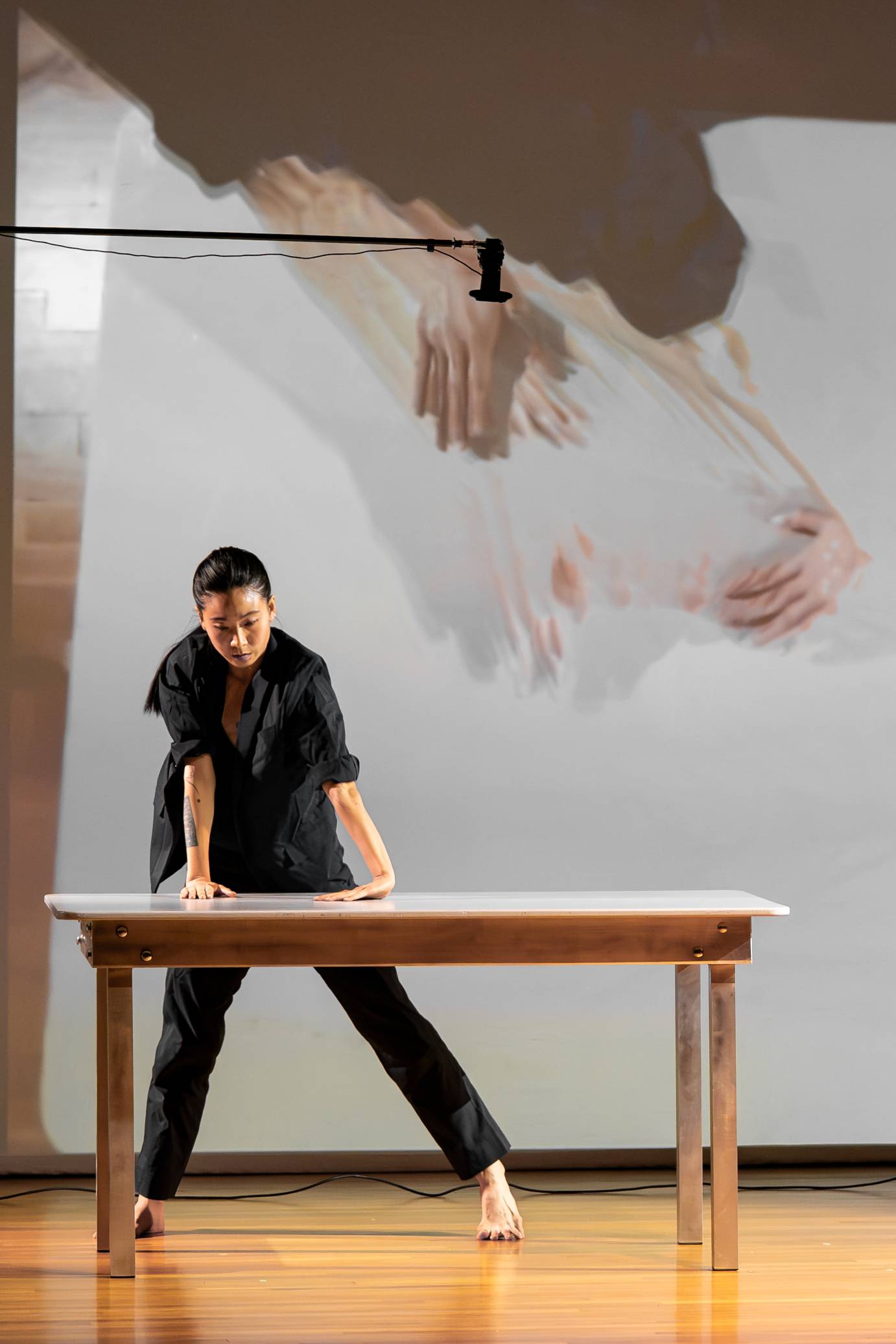 A woman stands behind a table, pressing her hands. Her hands are projected behind her.