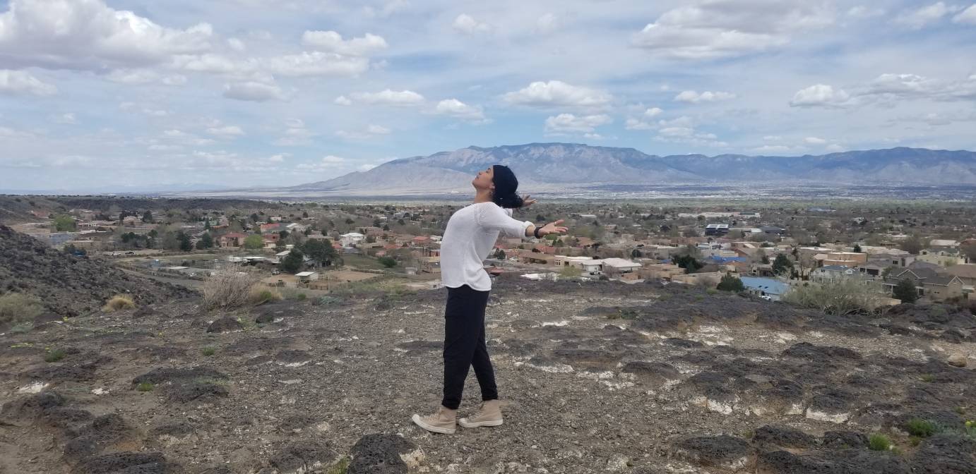 A dancer opens her arms wide against the panoramic background of the American Southwest