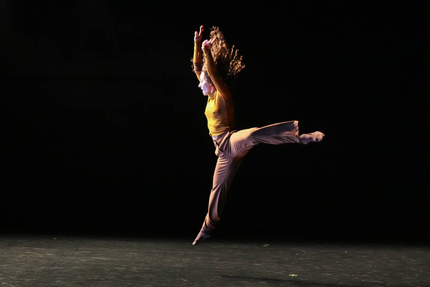 dancer's hairs fly up as she jumps into the air in a flying arabesque