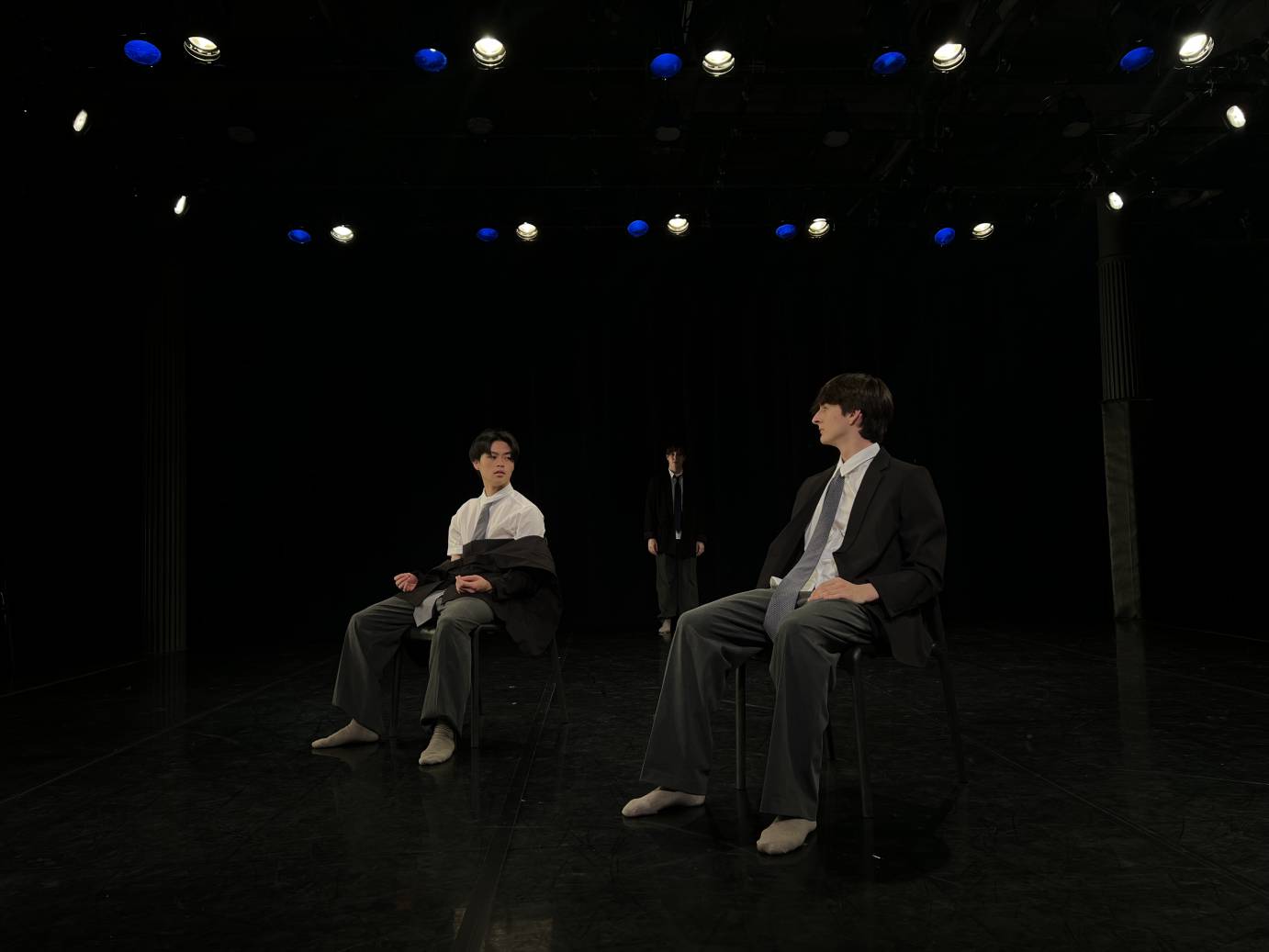 two men in suits seated parallel to one another stare at each other.