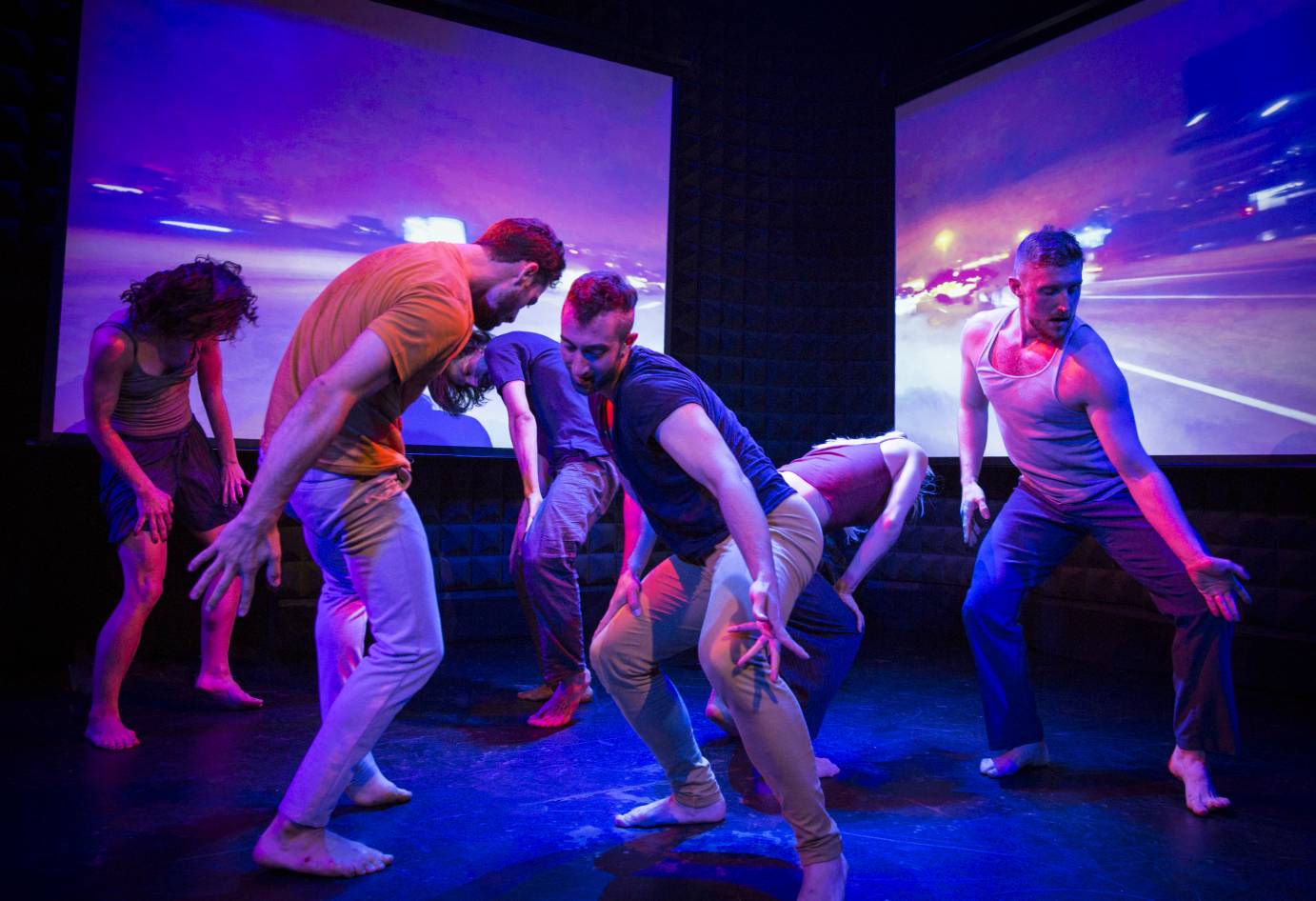 A group of dancers squat, one hand with fingers splayed