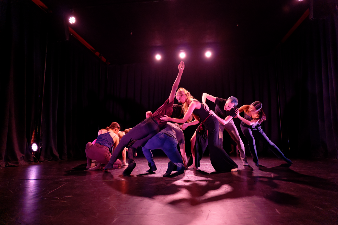 The dancers form an arc that rises from kneeling to standing. One person has fallen and is caught by the dancers behind him.