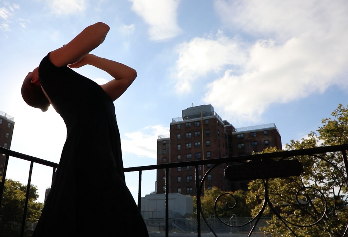 figure in black dress on fireescape reaching out to the blue ski