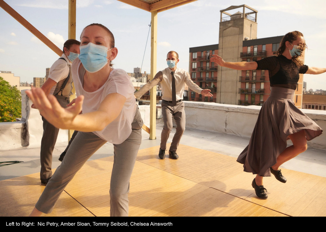 Four dancers in street clothes dance on a roof.