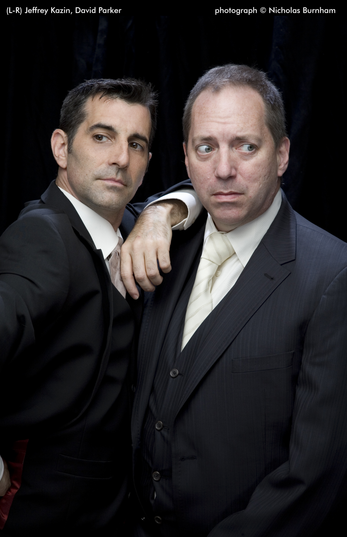 David Parker and Jeffrey Kazin wear suits, ties, and white shirts. Kazin has his arm on Parker's shoulder. Parker has a look of concern on his face.