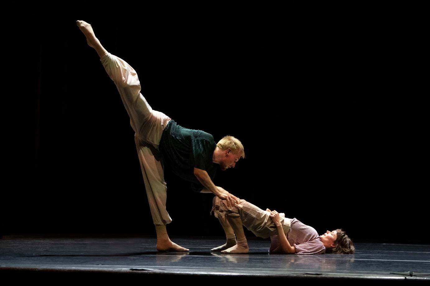 Alice Klock bridges her lower body off the ground. Florian Lochner penchees, lifting his leg high to the back, as he balances on her knees.