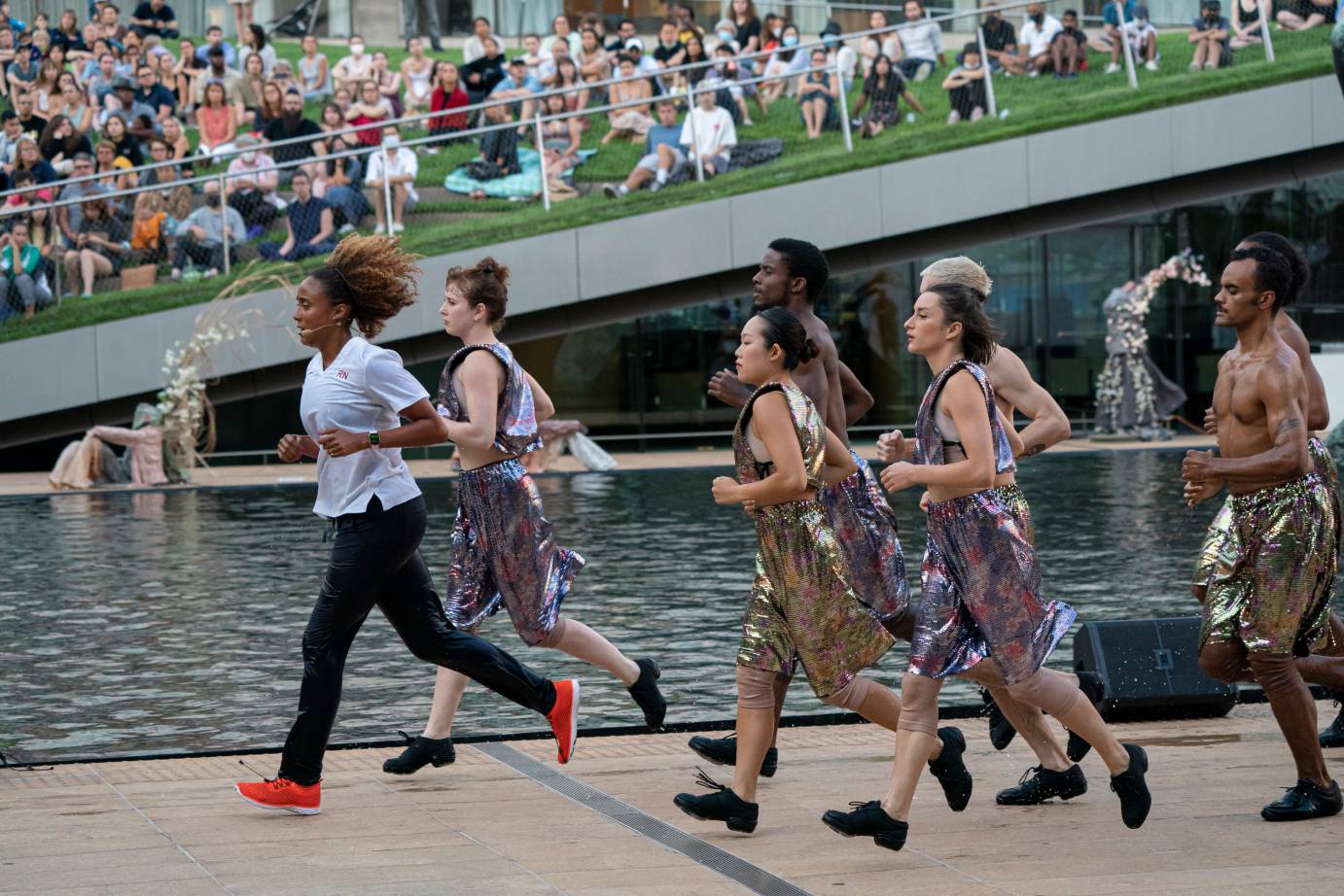 In red sneakers, Valarie Wong runs as a pack of metallic-clad dancers follow her