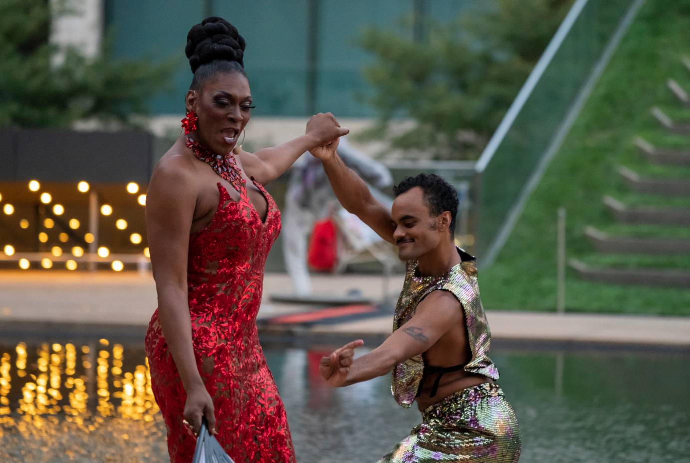 Egyptt LaBeija wears a red dress and holds Taylor Stanley's hand. Stanley extends his free arm sideways