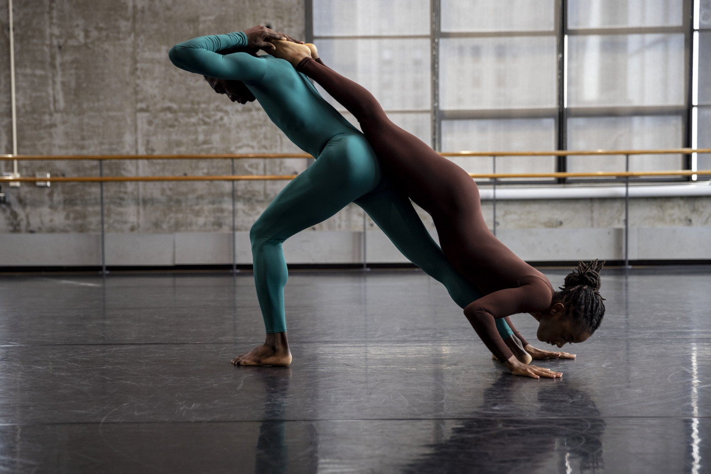 Chalvar Monteiro lunges in profile with Jacquelin Harris lying face first down his body. He holds her legs behind his neck.