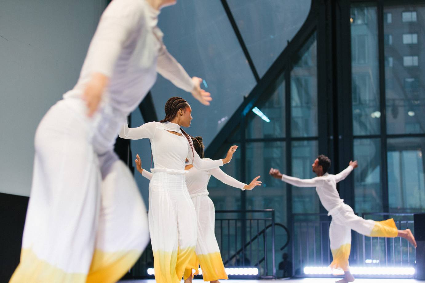 Three dancers extend their arms in low V's as Kyle Marshall chugs in profile, one leg lifted