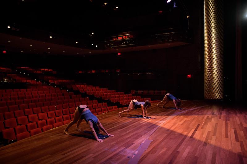 Three women crouch with their hands and feet on the ground while their haunches face out to the auditorium.