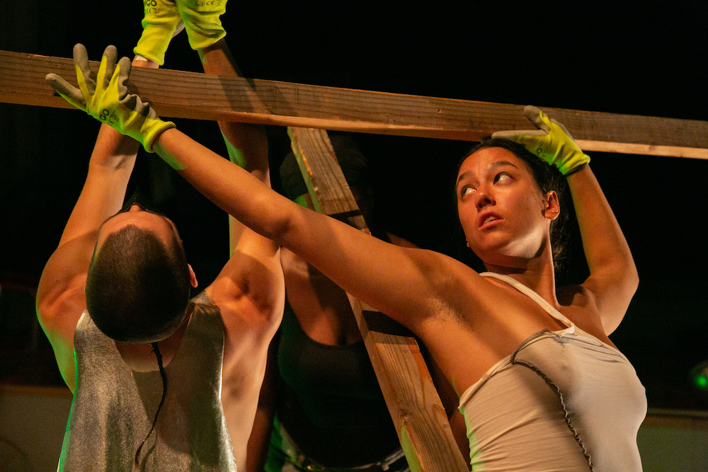 two figures hold and support beams as if they are building. They wear green construction gloves