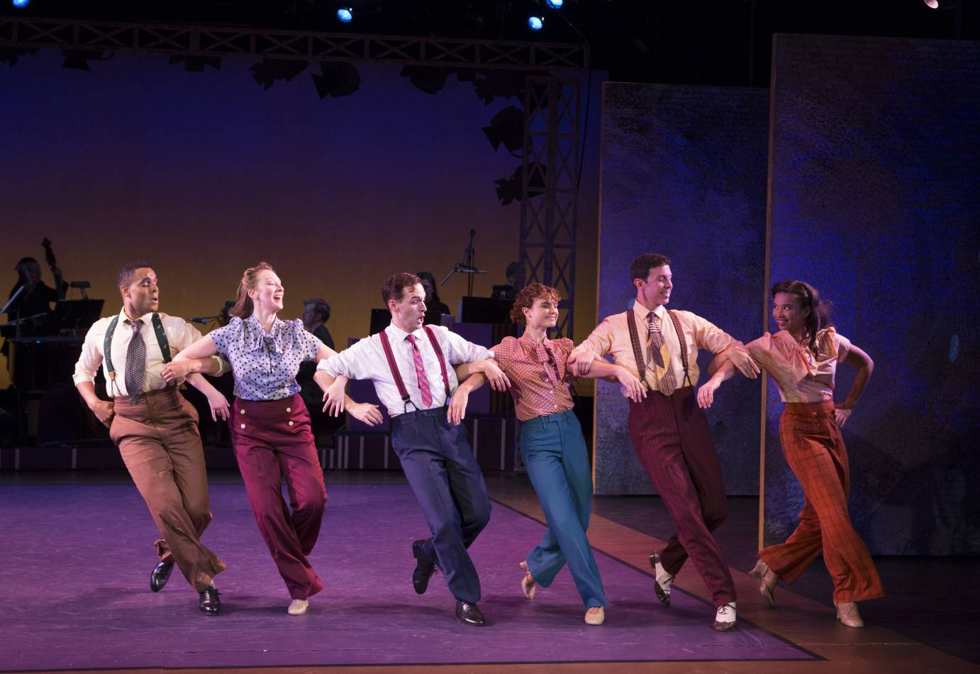A cast of three men and three women link elbows and extend one foot forward. The woman wear pussy-bow blouses while the men sport suspenders and neckties.