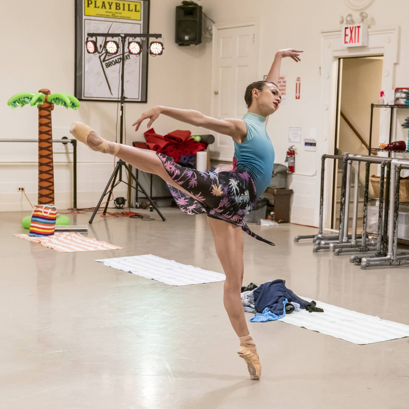 In a teal leotard and floral ballet skirt, a woman executes a lush arabesque
