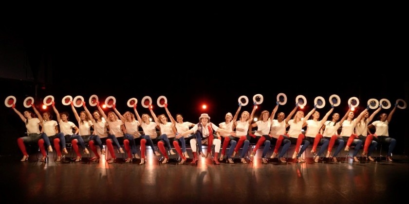 One man is flanked by two lines of kneeling dancers who've extended a hat-holding hand in the air.