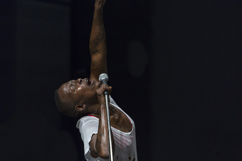 nora sings passionately into a microphone wearing a ripped white t-shirt