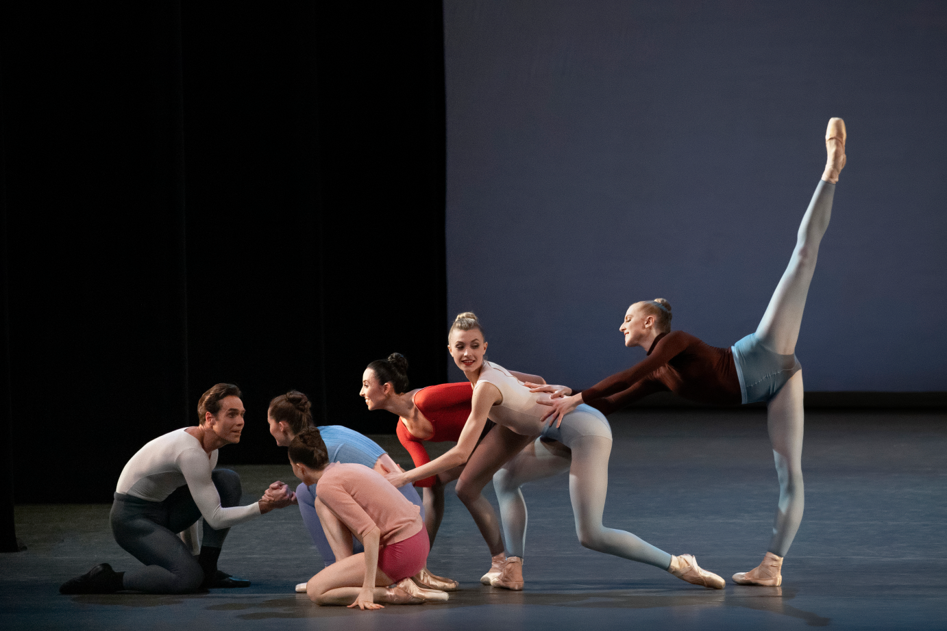 One man kneels. Behind him, women line up, with the one closest to the man kneeling, the next three crouch, and the last extends her leg in a high arabesque.