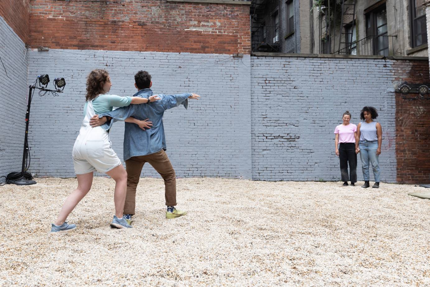 Two dancers with their arms wrapped around each other stand diagonally across from two dancers with their arms at their sides