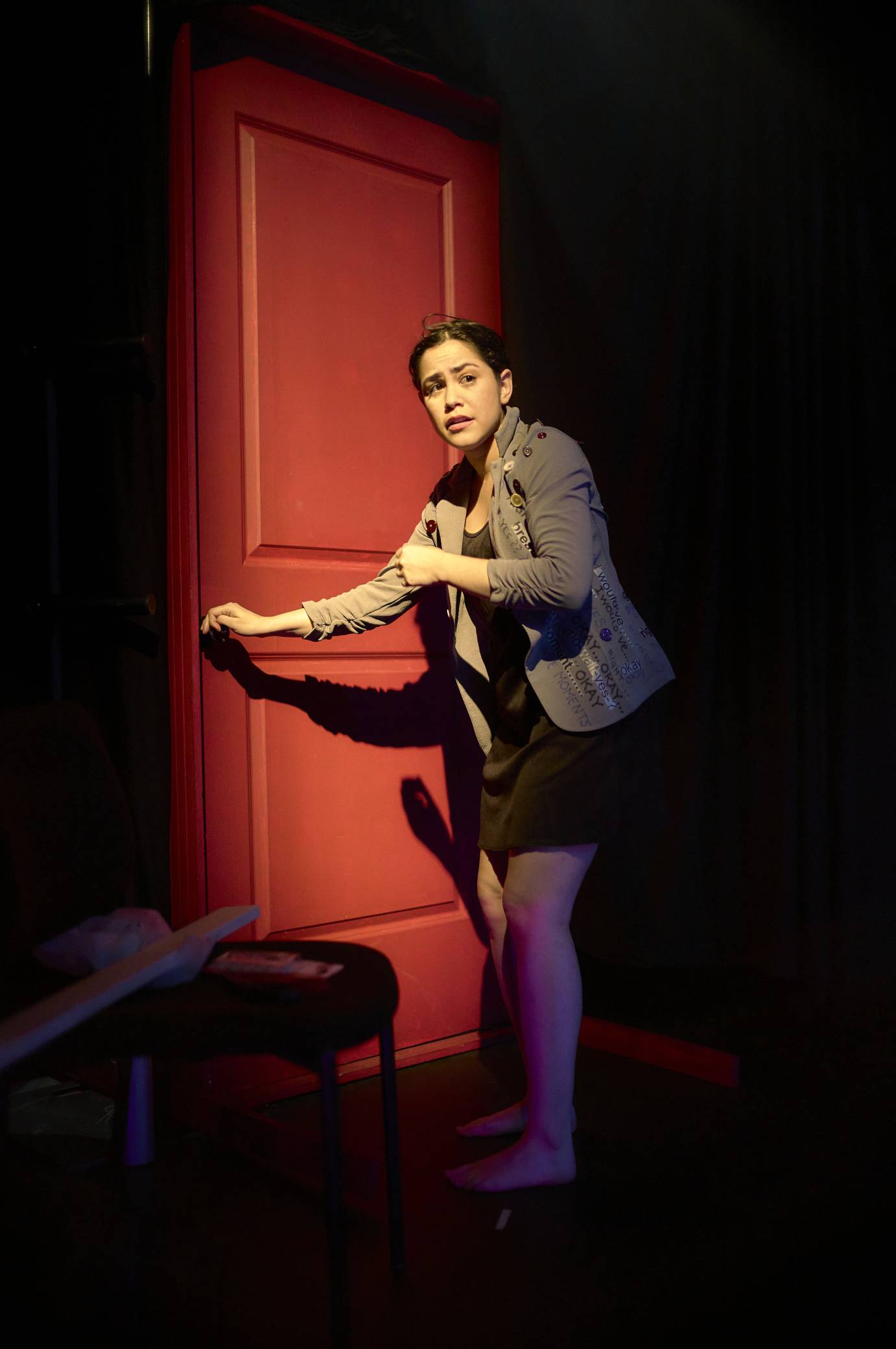 a young woman with a concerned look on her face approaches a red door to open it