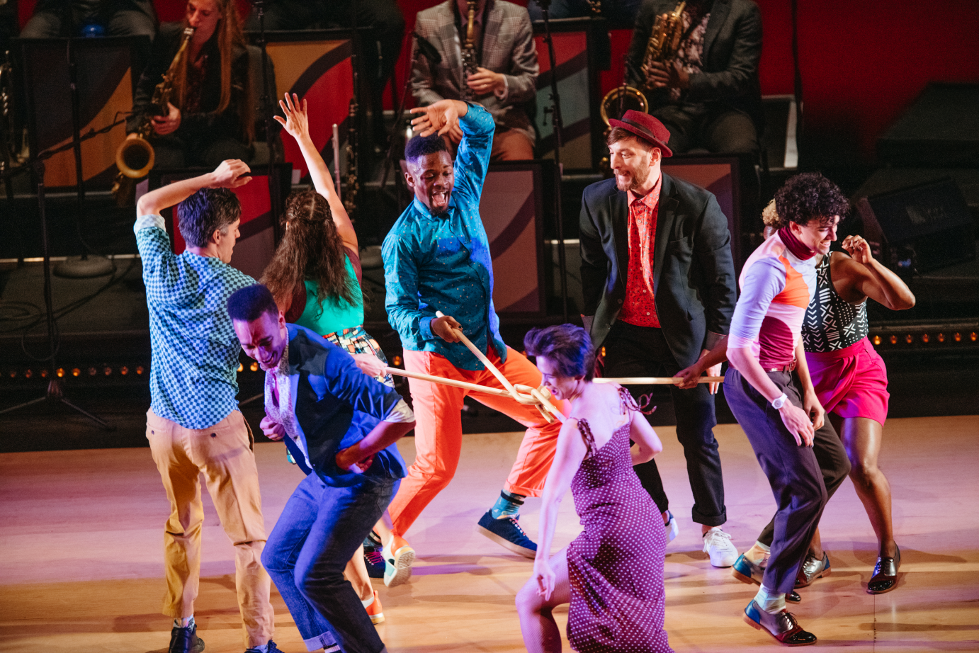 Grinning dancers link the top of canes, to evoke spokes on a wheel, as they groove in a circle.