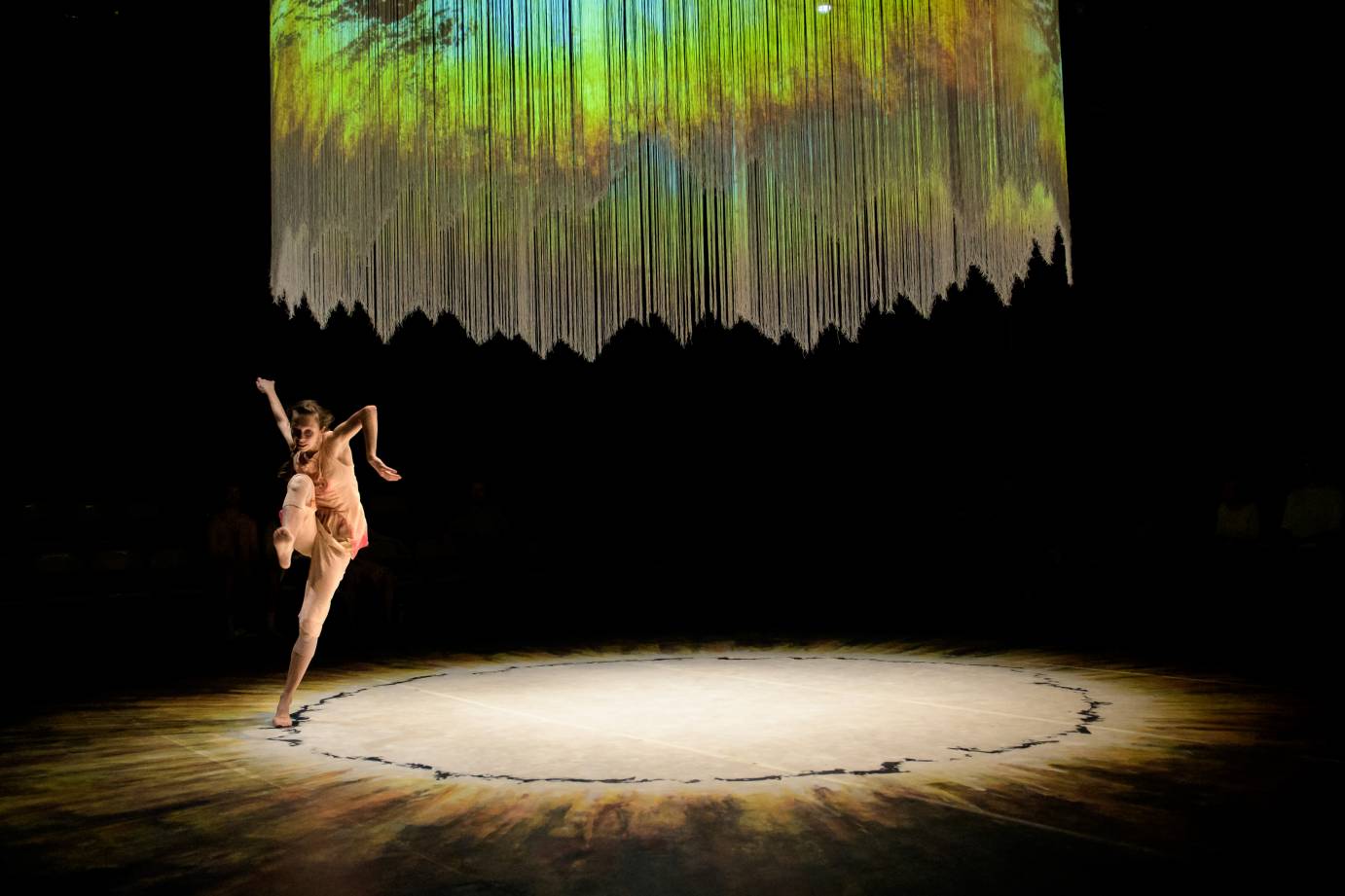 A woman swings her arm while one leg is flexed and bent in the air. The chandelier dangles above her.