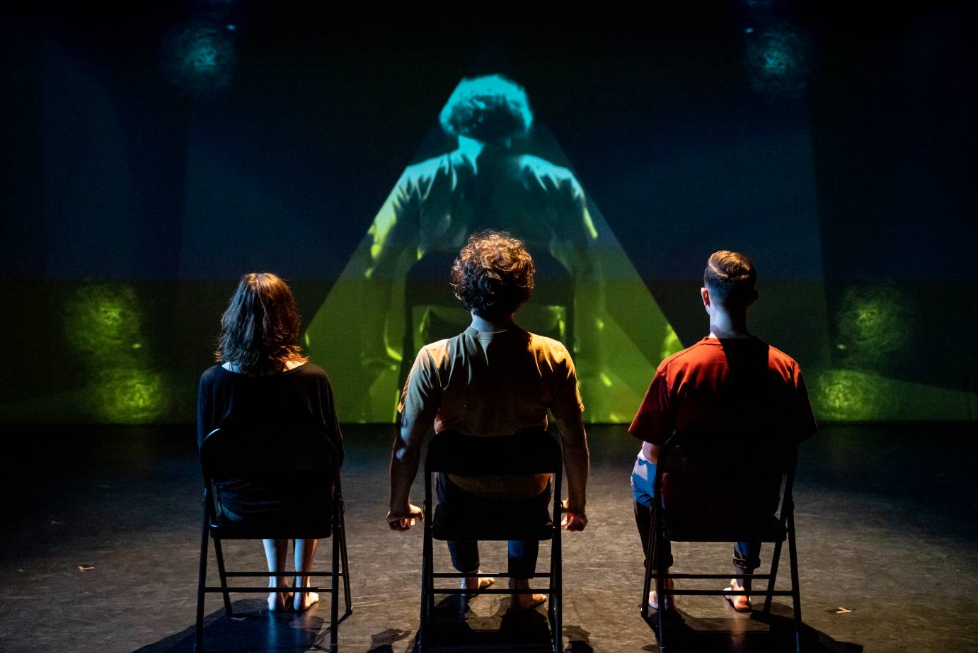 Three dancers watch a video. The video zooms in on the curly hair of one performer.